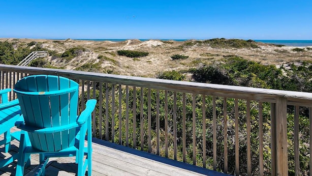 A wooden deck with a blue Adirondack chair overlooking a beach with dunes and the ocean. - Sand Dollar #13-HC: Oceanfront, Dog-Friendly, Private Hot Tub (Avon)