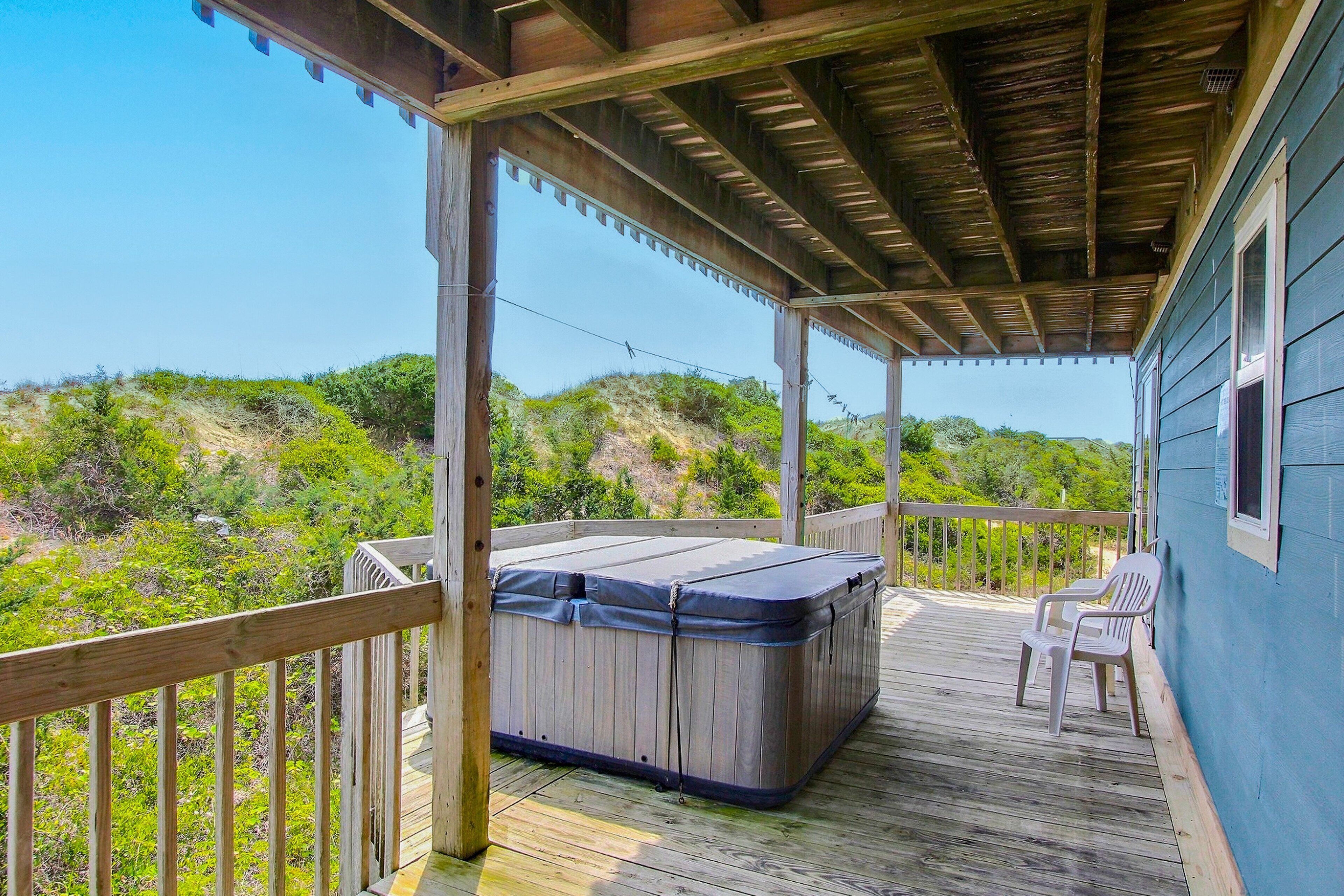 A wooden deck with a hot tub and two chairs, overlooking a hillside.