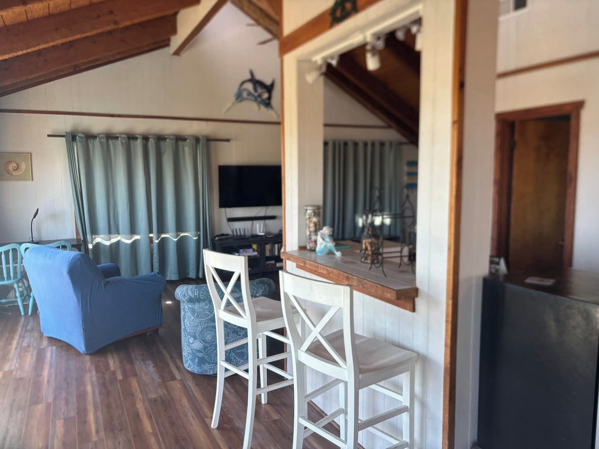 Una sala de estar acogedora con un sofá azul, sillas blancas, una mesa de centro de madera y un televisor al fondo.