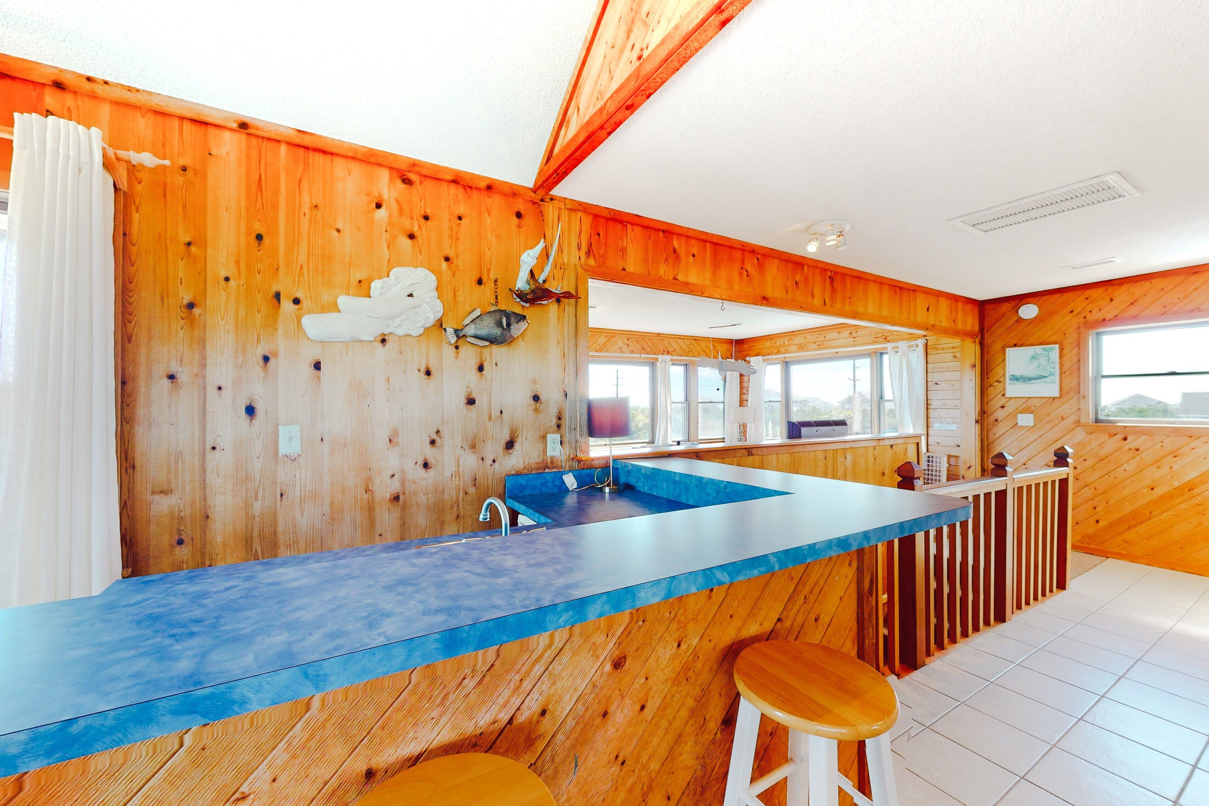 A kitchen with wooden walls, a blue countertop, and a large window.