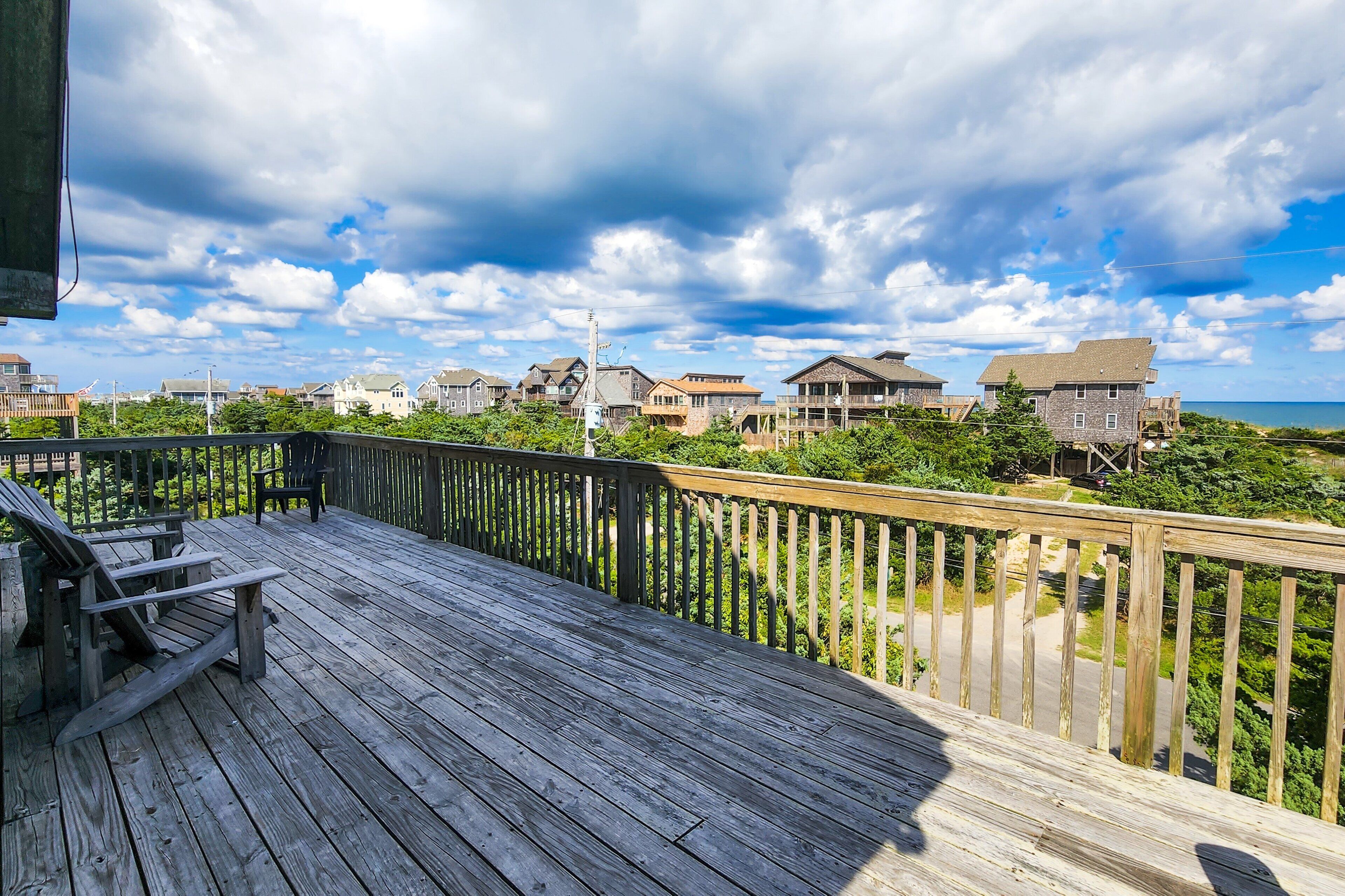 A wooden deck with a bench, overlooking a coastal area with houses and a view of the sea.