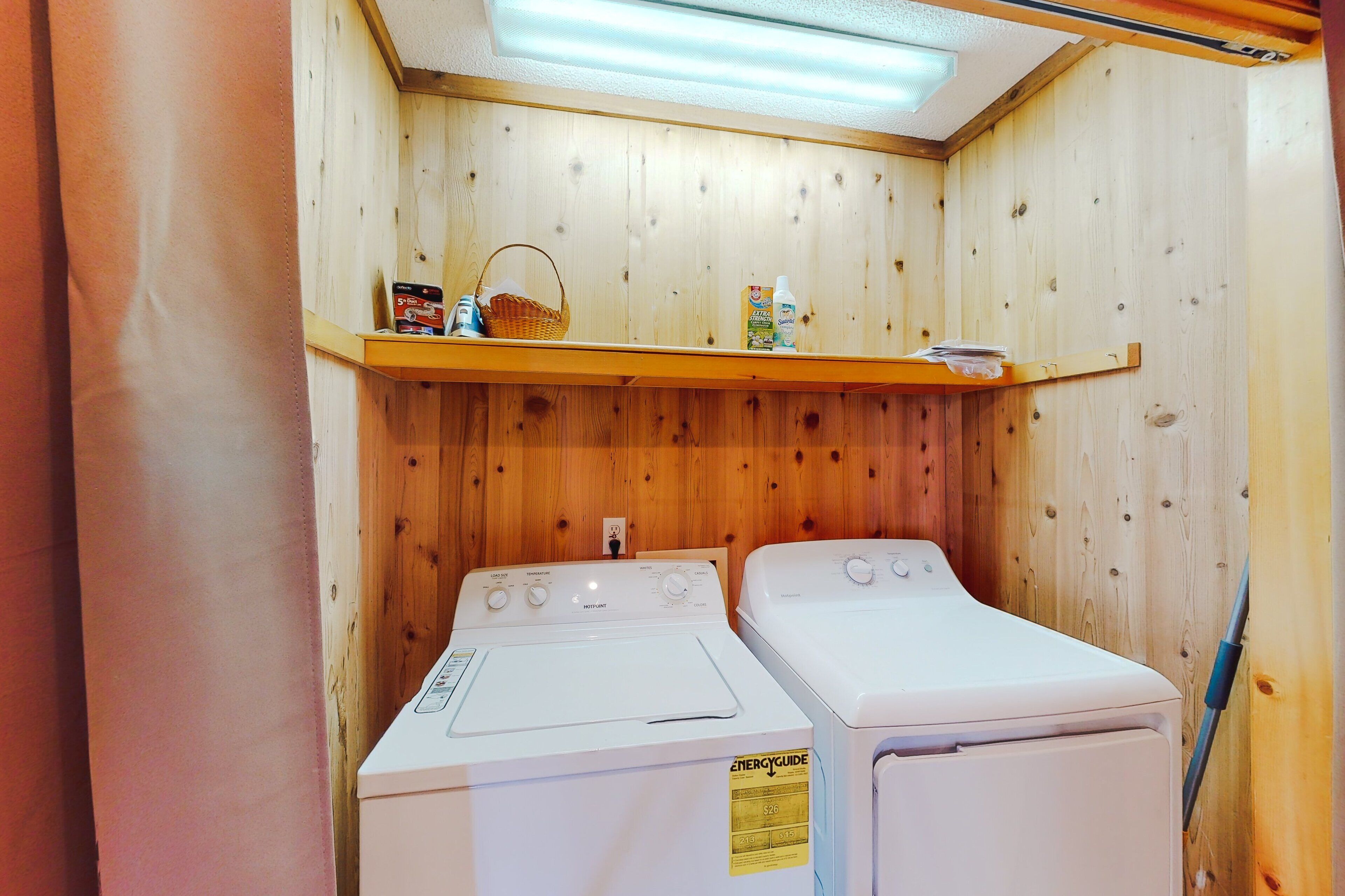 A laundry room with two white front-loading washing machines, a shelf with laundry supplies, and wooden paneling on the walls.