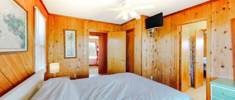 A wooden-paneled bedroom with a bed, a ceiling fan, a television, and a dresser.