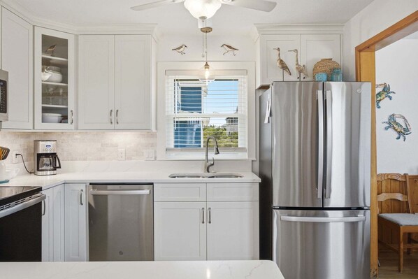 A modern kitchen with white cabinets, stainless steel appliances, a built-in dishwasher, and a window with blinds.
