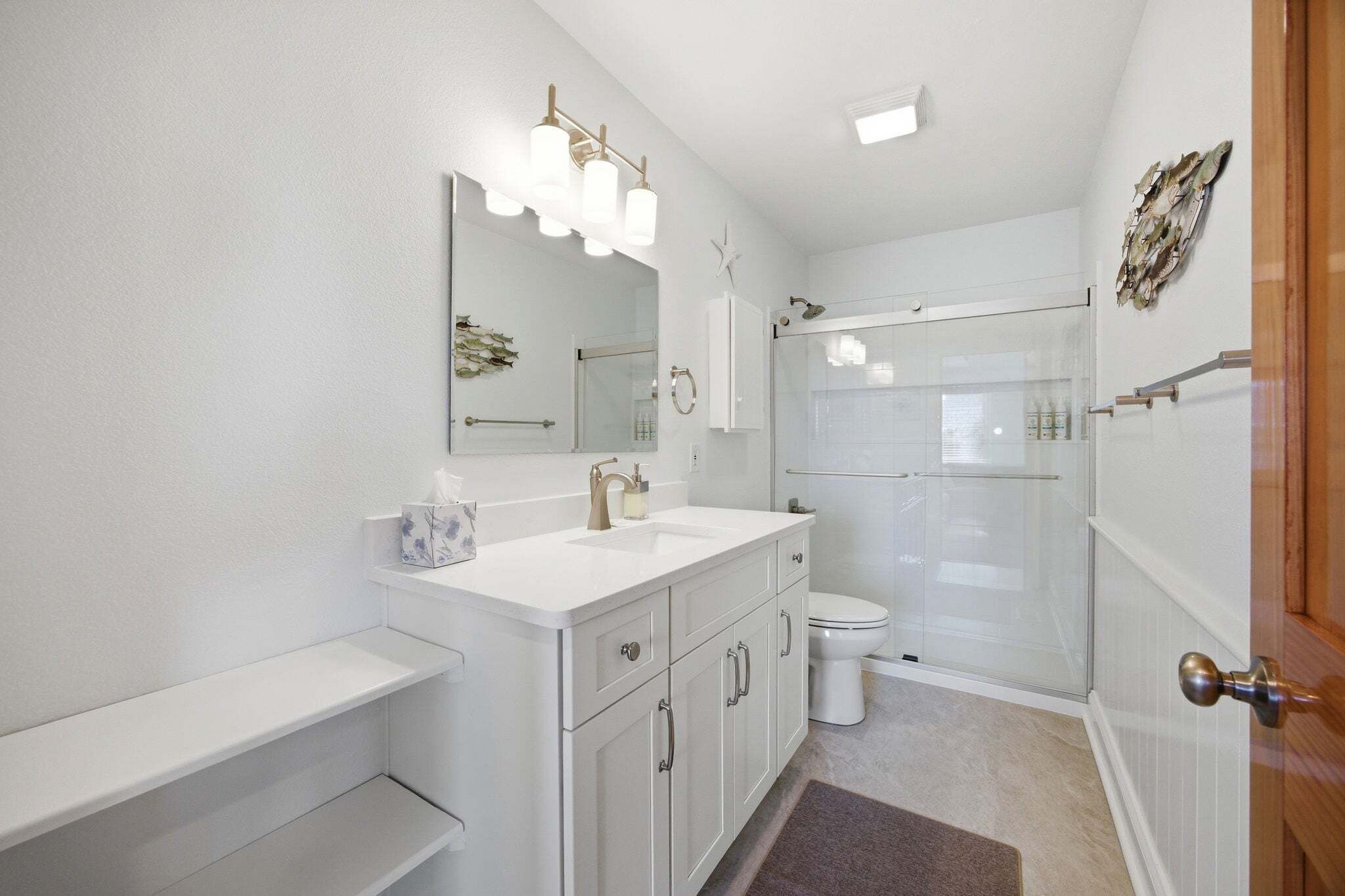 A bathroom with a white vanity, a glass shower enclosure, and a white toilet.
