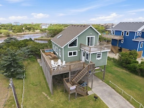 A two-story house with a deck, a hot tub, and a sign indicating it's for sale.