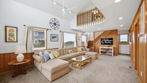 Un salón amplio con un sofá modular grande, una escalera de madera y un cartel que dice 'Hatteras Realty'.