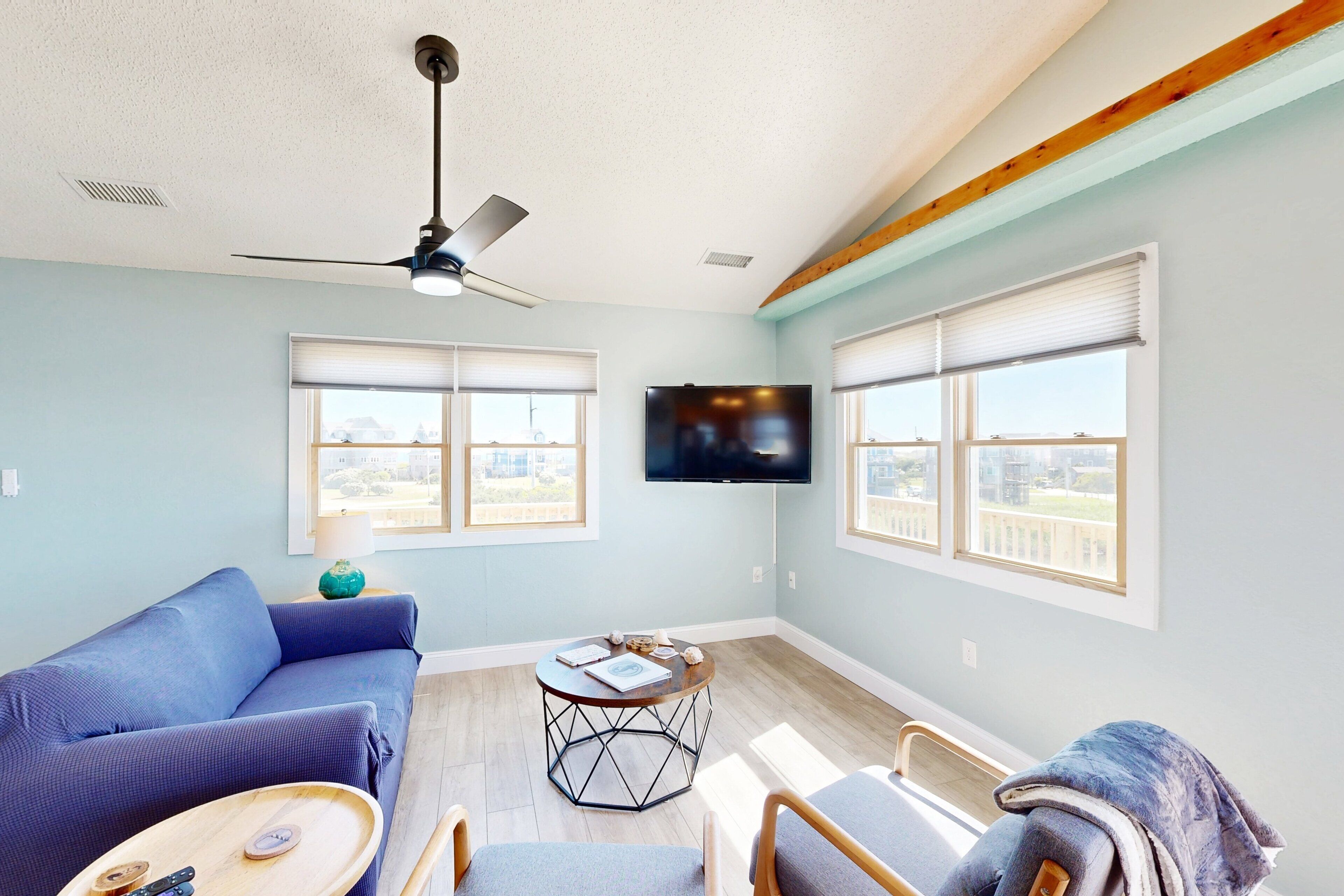 Un salon avec un canapé bleu, une table basse ronde, un ventilateur de plafond et un téléviseur fixé au mur.