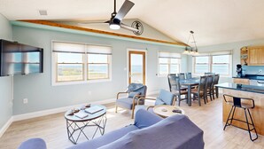 Amplia sala de estar con un sofá grande, mesa de comedor y sillas, cocina con barra y ventilador de techo.