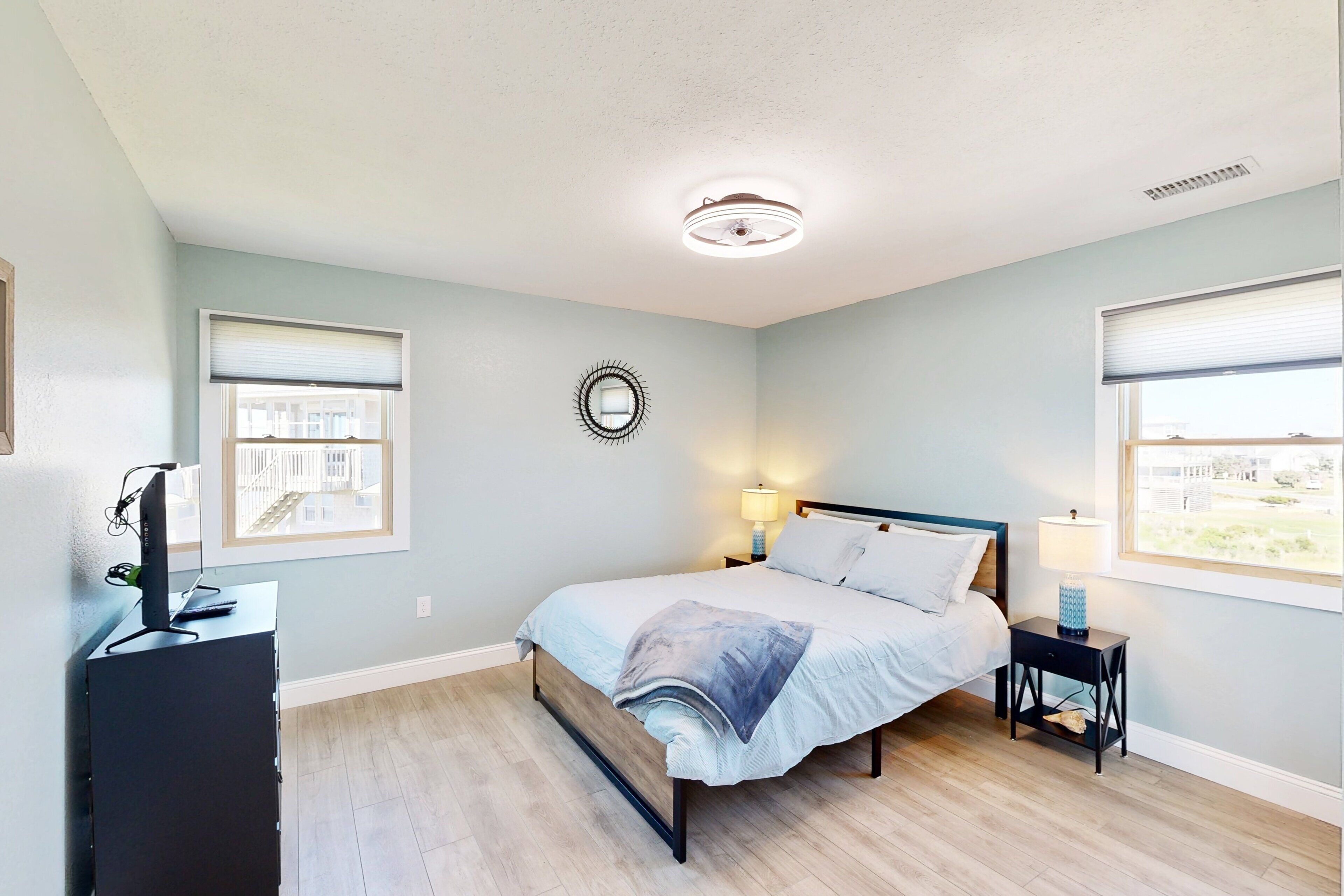 A bedroom with a bed, bedside tables, a desk with a computer, and a window.