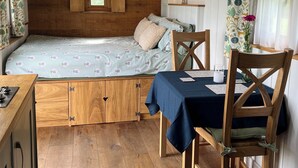 A compact room with a bed, a table, chairs, a TV, and a window with curtains. - Luxury Shepherd Hut with Private Hot Tub & Views of the Somerset Levels (Langport)