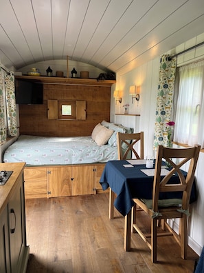 Ein kleines Zimmer mit Bett, Tisch, Stühlen, Fernseher und einem fenster mit Vorhängen.
