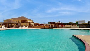 Una piscina con agua cristalina azul, rodeada por una terraza de madera y sillones de descanso.