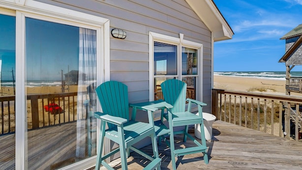 Terraza de madera con dos sillas y una mesa, con vista a la playa.