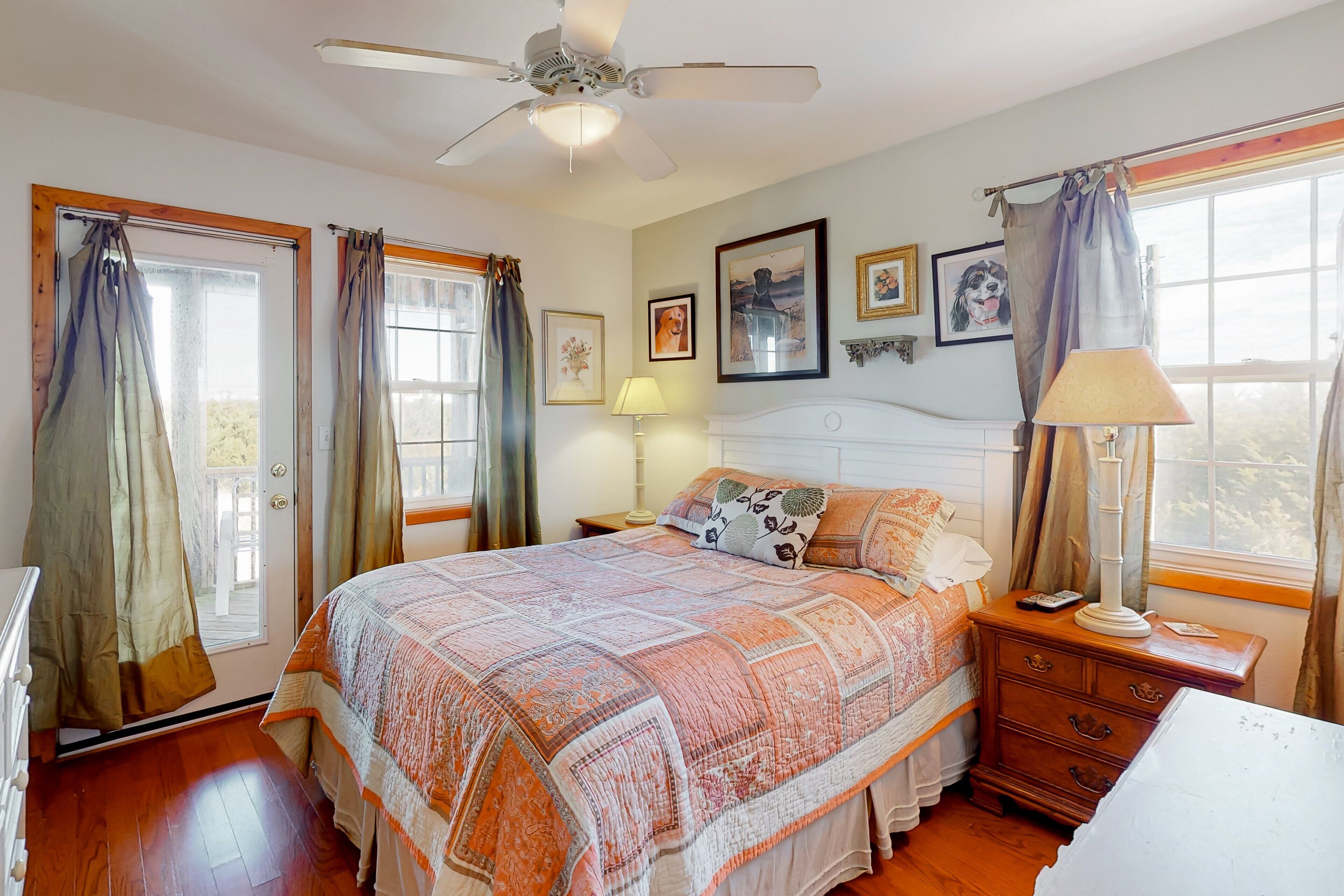 A bedroom with a bed, nightstands, a ceiling fan, and framed pictures on the wall.