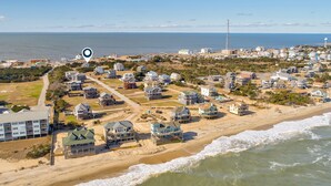 Una vista aerea di una zona residenziale costiera con case vicino alla spiaggia, un cielo sereno e l'oceano sullo sfondo.