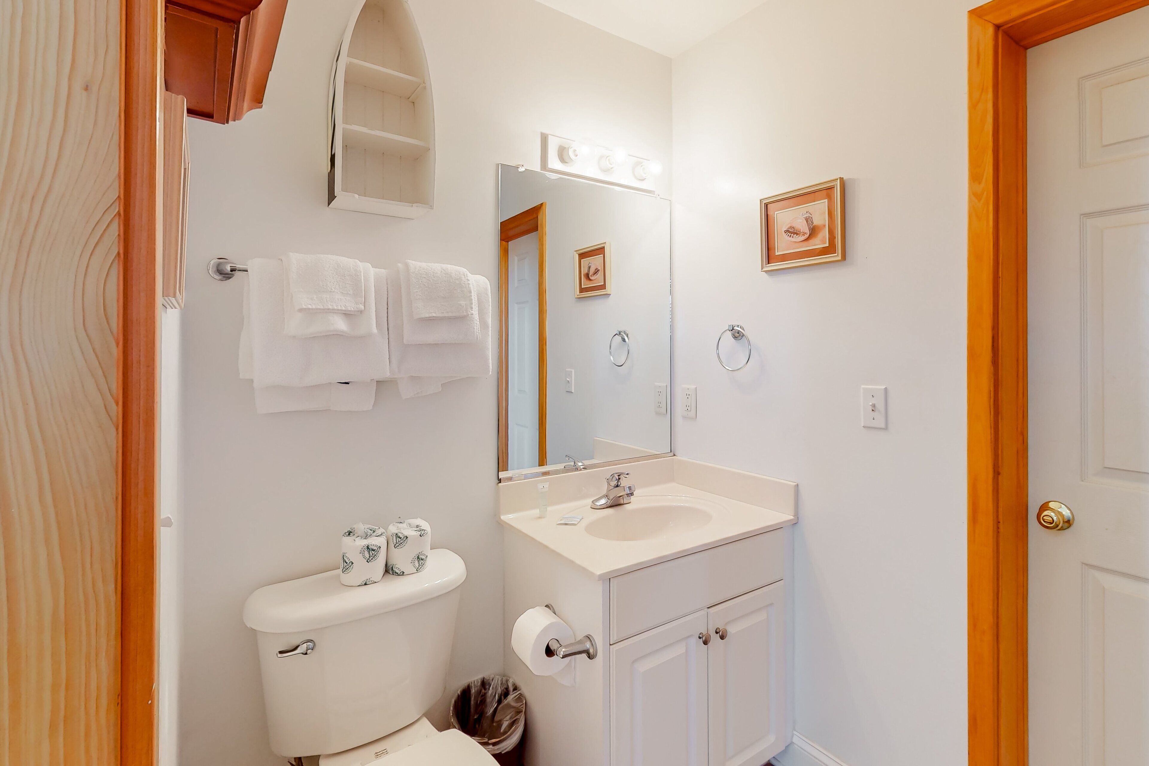 A bathroom with a toilet, sink, and mirror. There are towels hanging on the wall and a trash can.