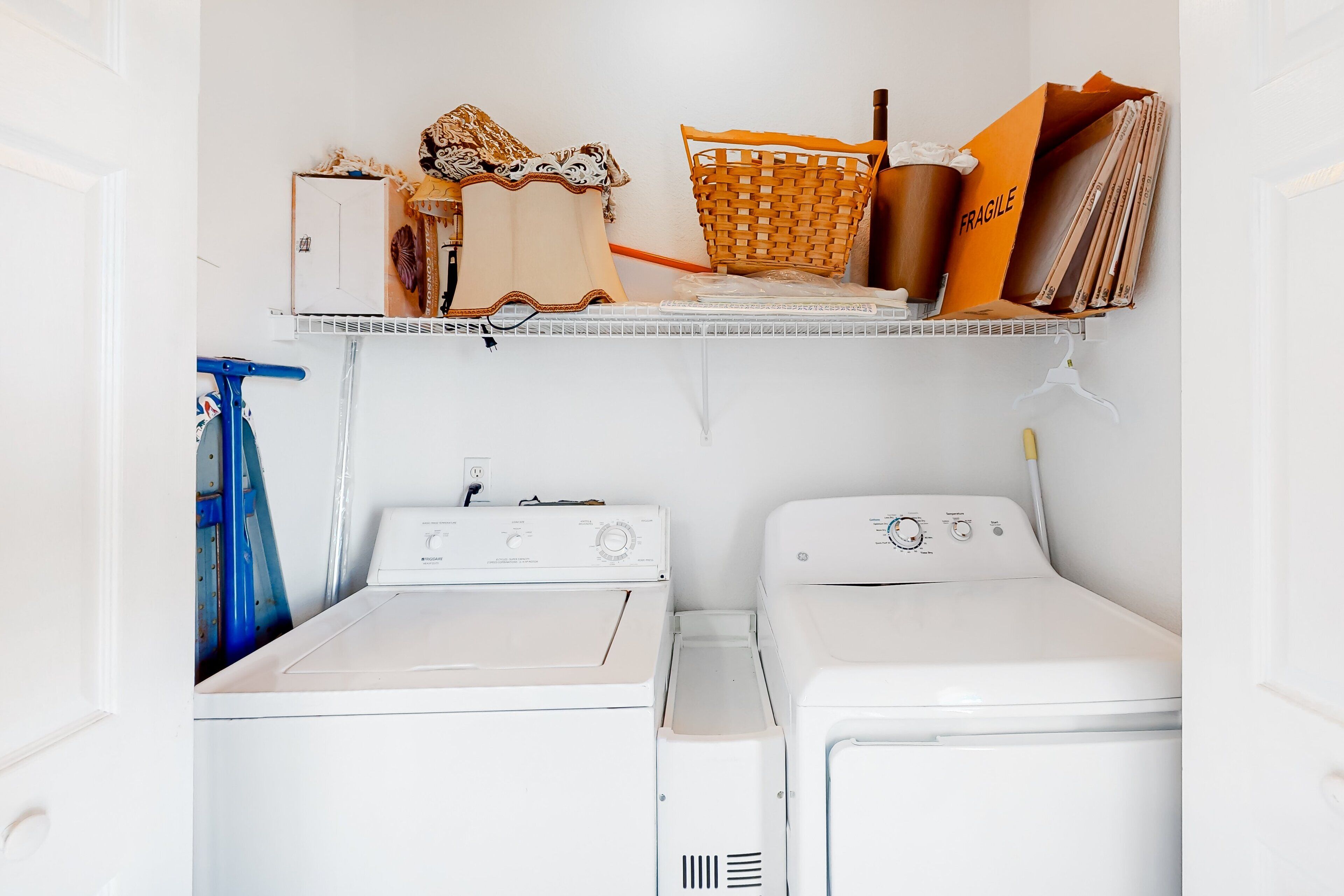 A laundry room with two white washers and dryers, a shelf with various items, and a blue mop.