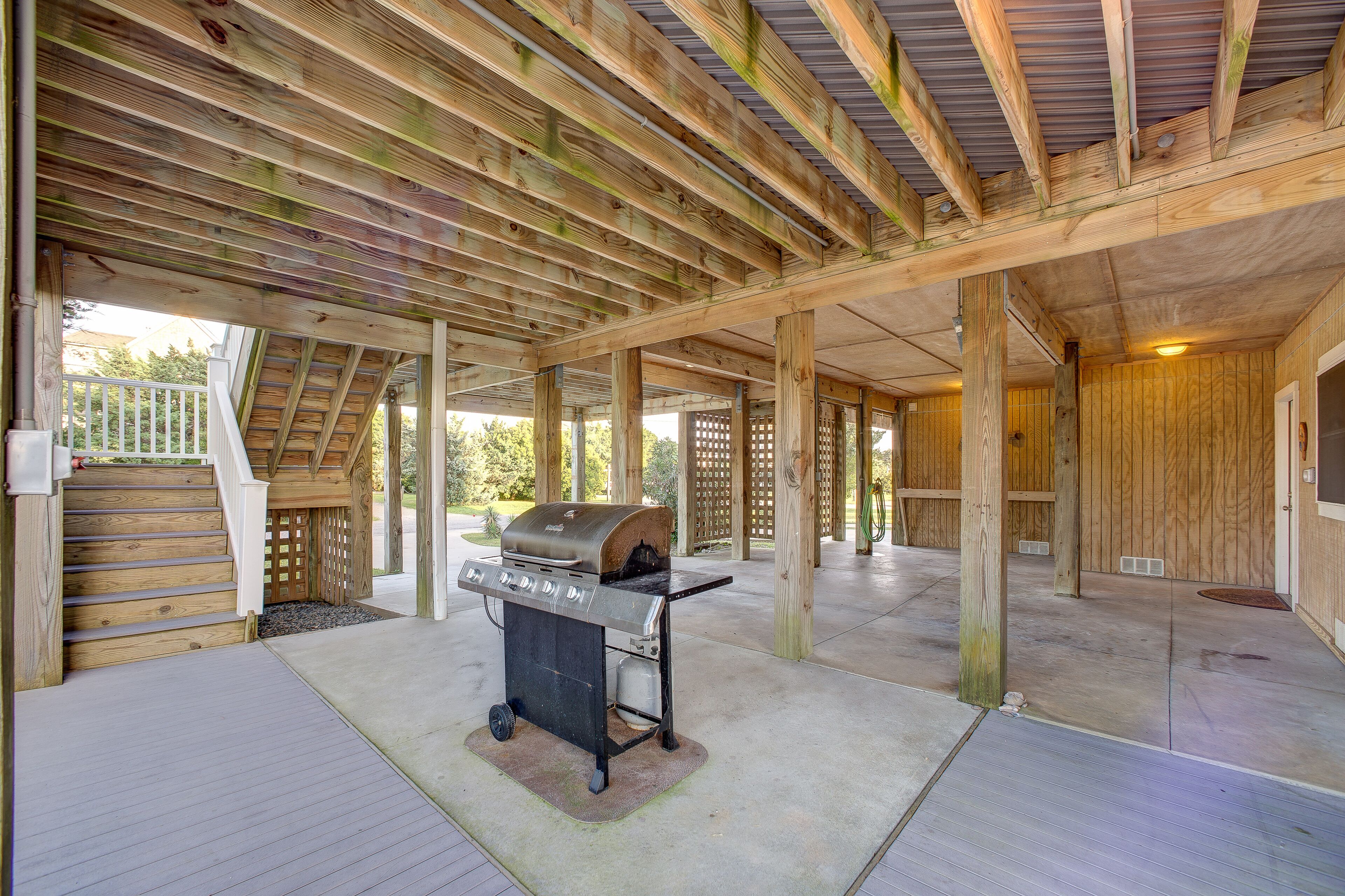 Un patio techado al aire libre con una estación de barbacoa, vigas de madera y piso de concreto.