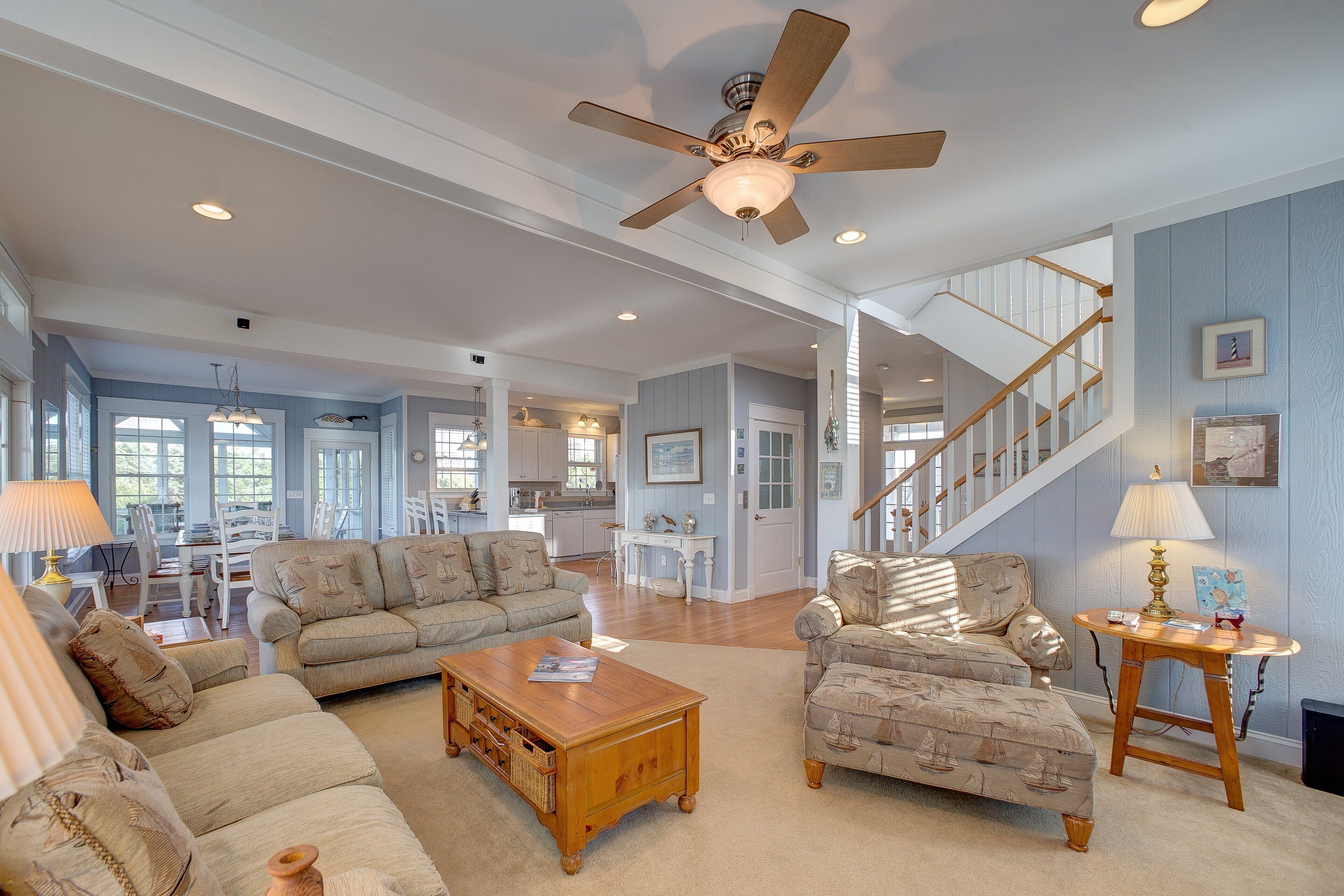 A spacious living room with a ceiling fan, a wooden coffee table, and two patterned armchairs.