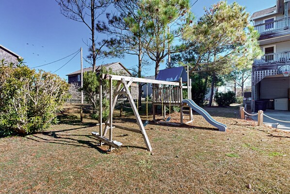 A playground with a swing set and slide, surrounded by trees and residential buildings.