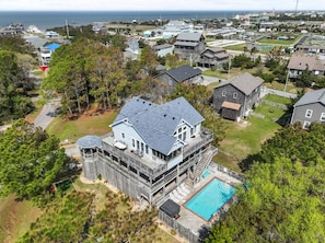 A large house with a pool, surrounded by trees and other houses.