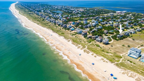 Vue aérienne d’une zone résidentielle côtière, avec des maisons, une plage et une vaste étendue d’eau.