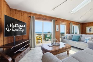 A living room with a TV, wooden walls, a sofa, a coffee table, and a view of the sea.