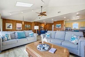 A spacious living area with two grey sofas, a wooden coffee table, and a ceiling fan.