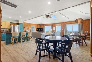 A spacious living area with a dining table, chairs, a sofa, and a kitchen area with a refrigerator.