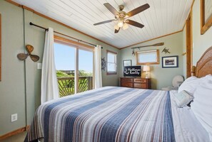 A bedroom with a bed, ceiling fan, window with curtains, and a sign for 'Hatteras Realty.'