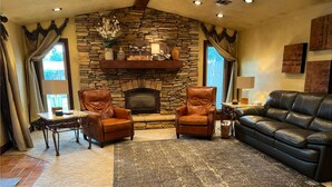 A living room with a stone fireplace, leather armchairs, a black leather sofa, and a coffee table. - Homestead Hideaway (Sentinel)