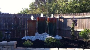 A garden with two tall, narrow planters, a stone wall, and a wooden fence. - Homestead Hideaway (Sentinel)