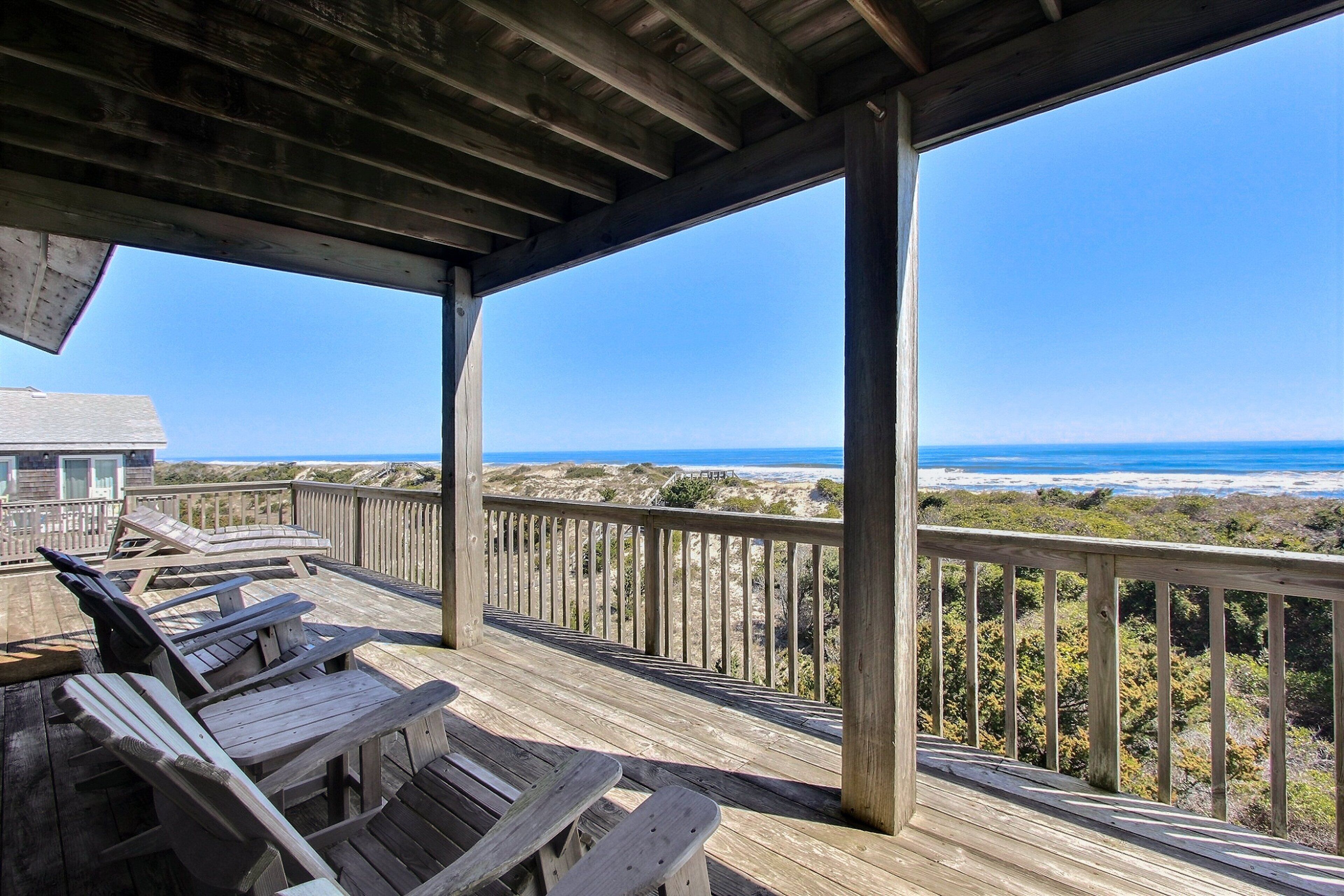 Une terrasse en bois avec des chaises longues donnant sur une plage.