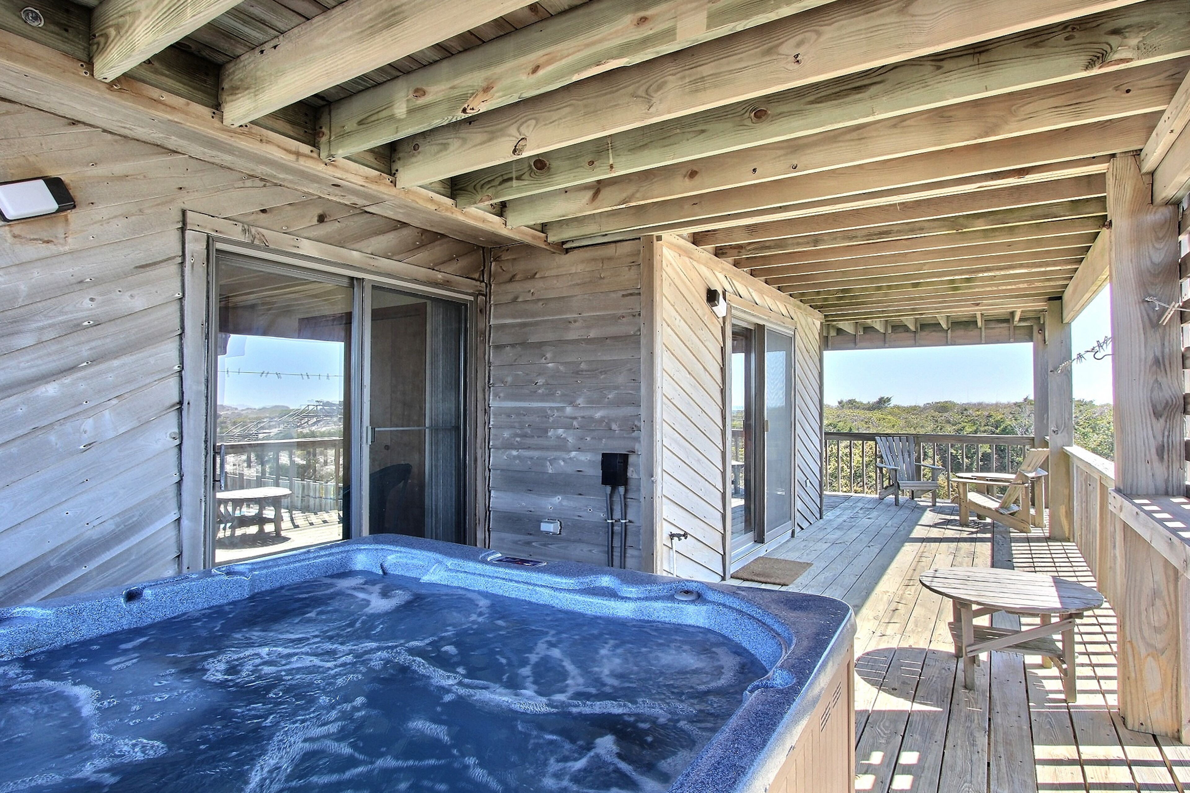 Een houten terras met een jacuzzi, buitenmeubels en uitzicht op het landschap.