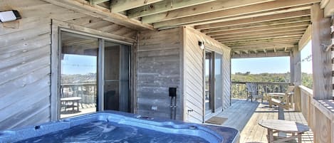 Een houten terras met een jacuzzi, buitenmeubels en uitzicht op het landschap.