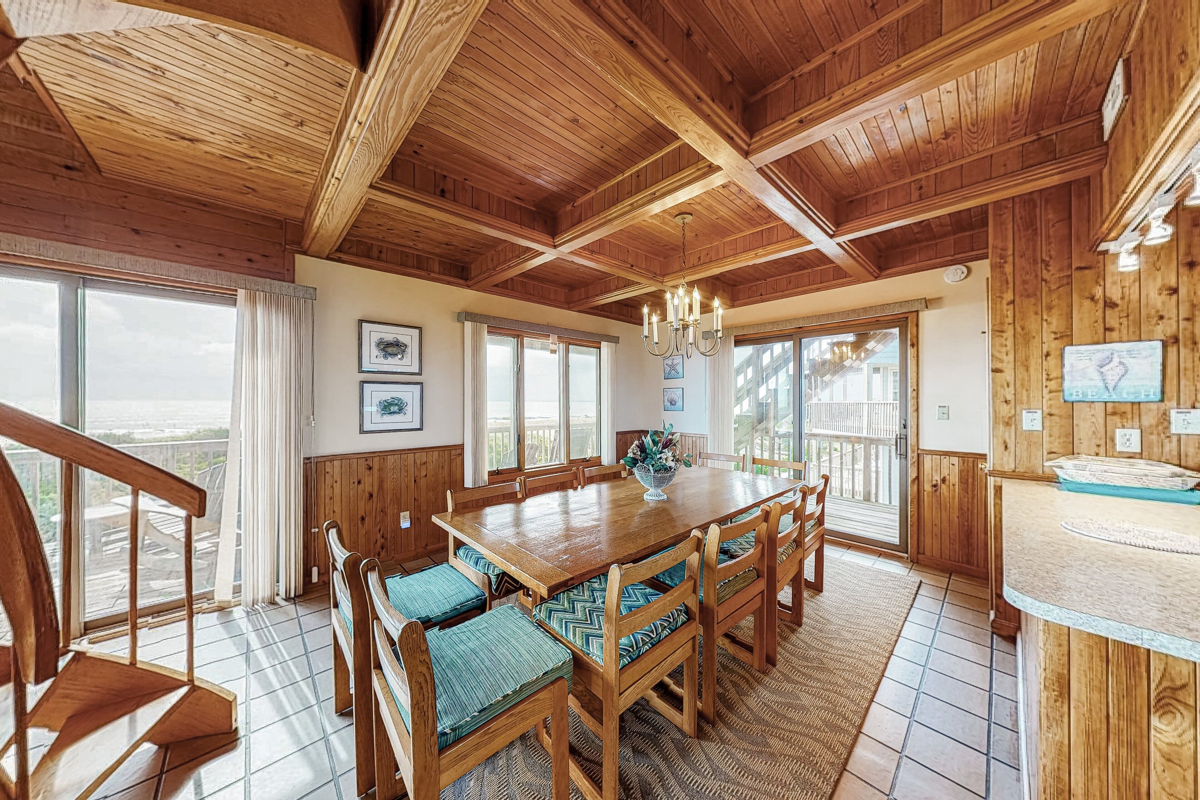A wooden dining room with a large table and chairs, a chandelier, and large windows.