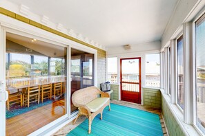 Une terrasse couverte avec un fauteuil en osier, une table à manger avec des chaises et une porte rouge.