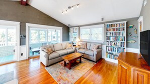 A spacious living room with a large sectional sofa, a wooden coffee table, and a bookshelf filled with books. - Reel Paradise: Steps From Canal w/Screened-in Porch (Avon)