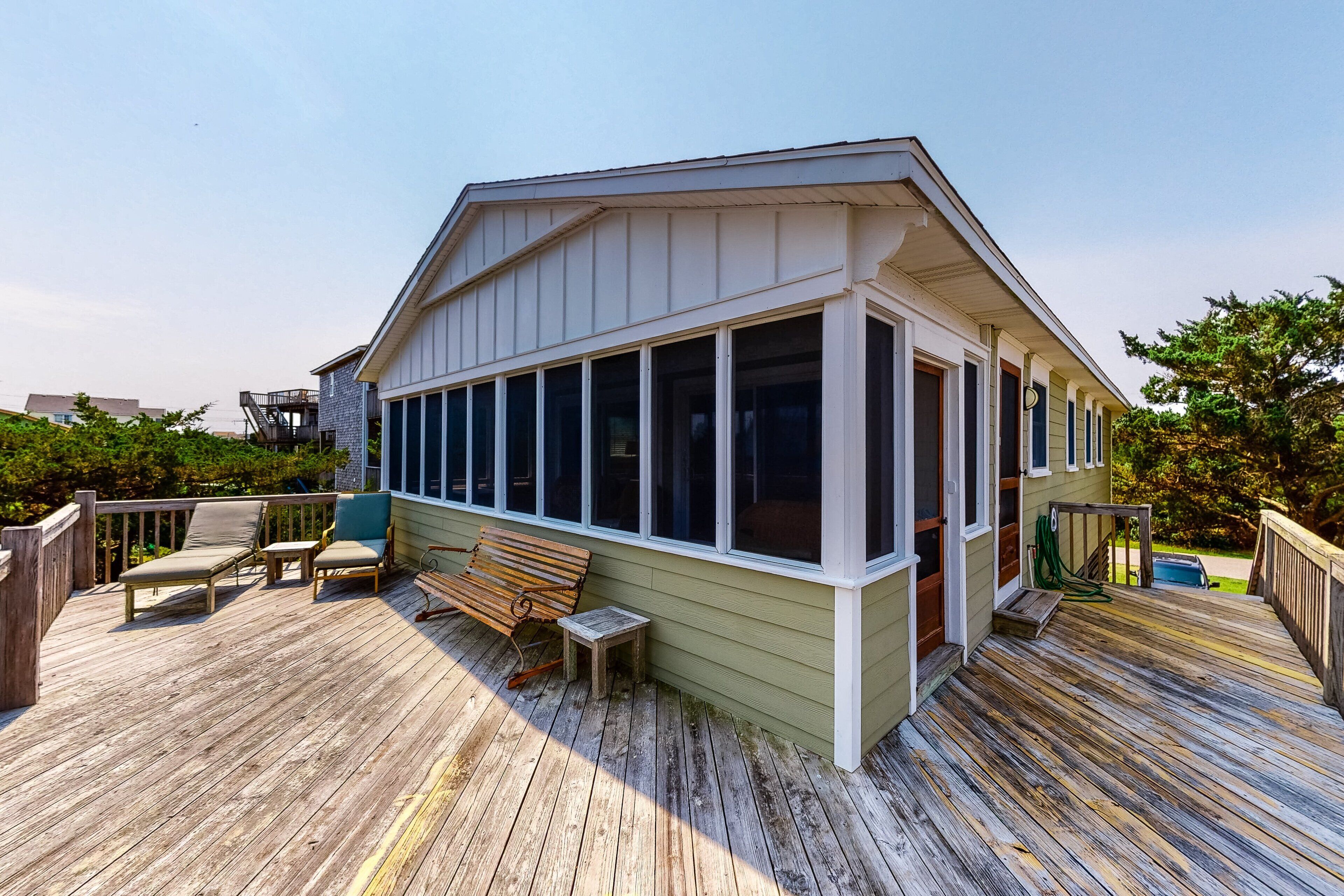 A wooden deck with outdoor seating, a covered area with large windows, and a small table.