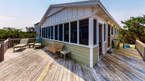 A wooden deck with outdoor seating, a covered area with large windows, and a small table. - Reel Paradise: Steps From Canal w/Screened-in Porch (Avon)