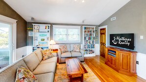 A living room with a sofa, a coffee table, a TV, and a bookshelf. - Reel Paradise: Steps From Canal w/Screened-in Porch (Avon)