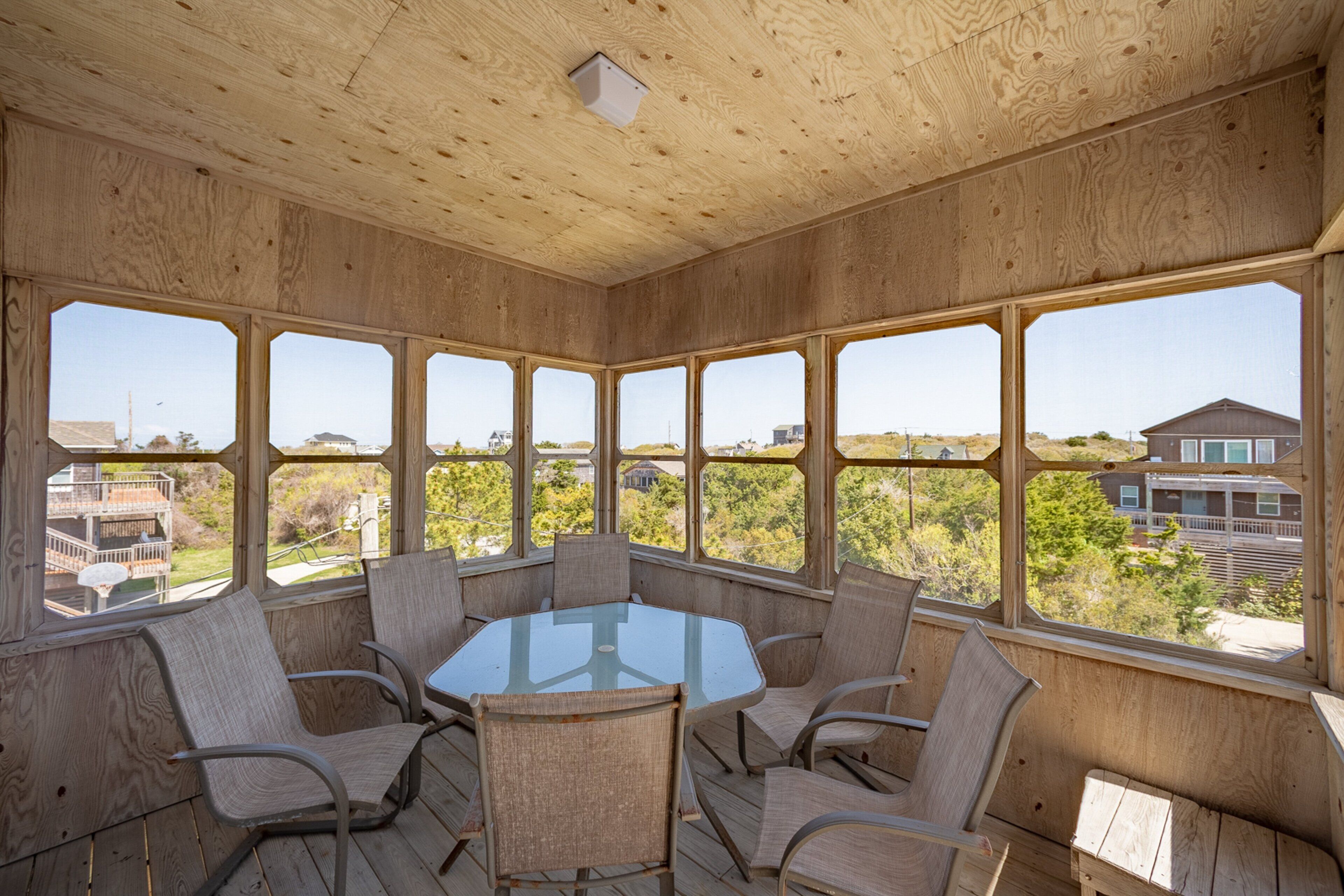 A wooden-paneled room with a glass table and chairs, large windows, and a view of a residential area.