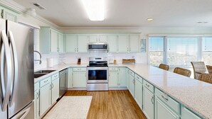 A modern kitchen with light green cabinets, stainless steel appliances, and a large island with seating. - Sunset Park: Short Walk to the Beach, Great Views (Avon)