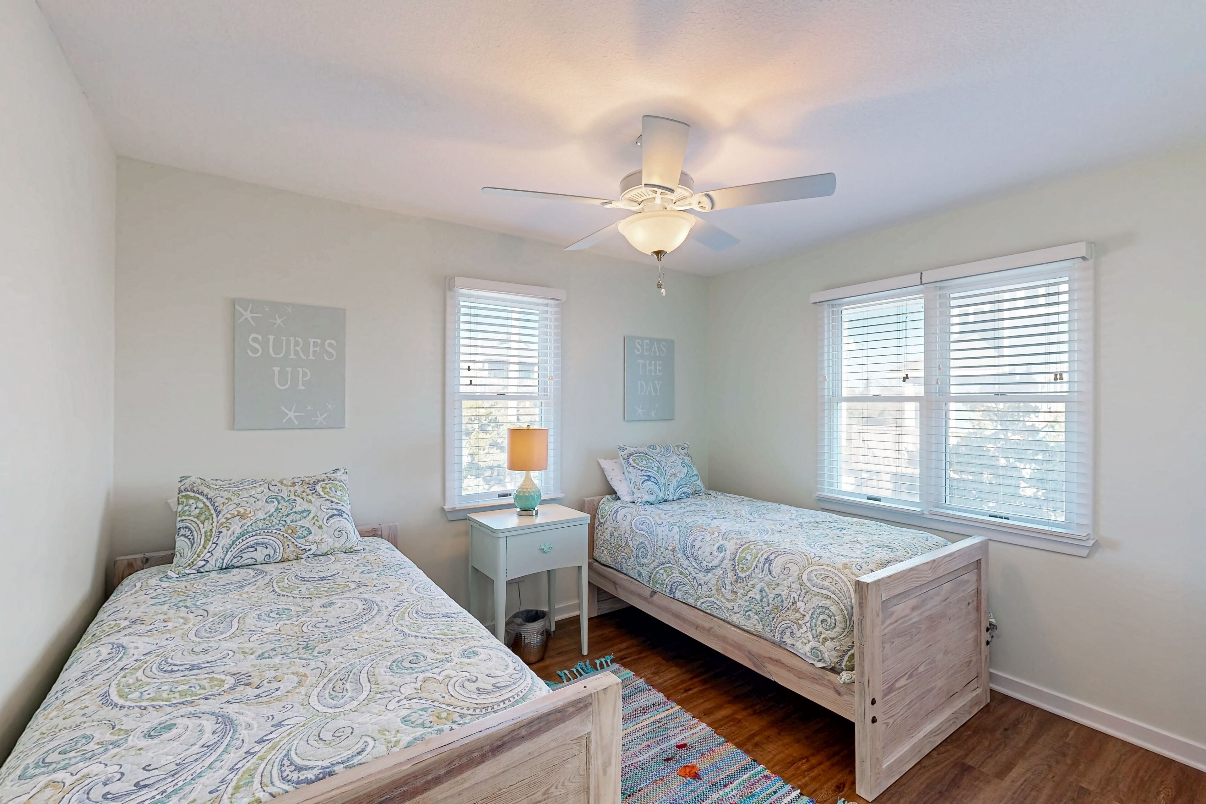 A bedroom with two single beds, a ceiling fan, and two windows with blinds.