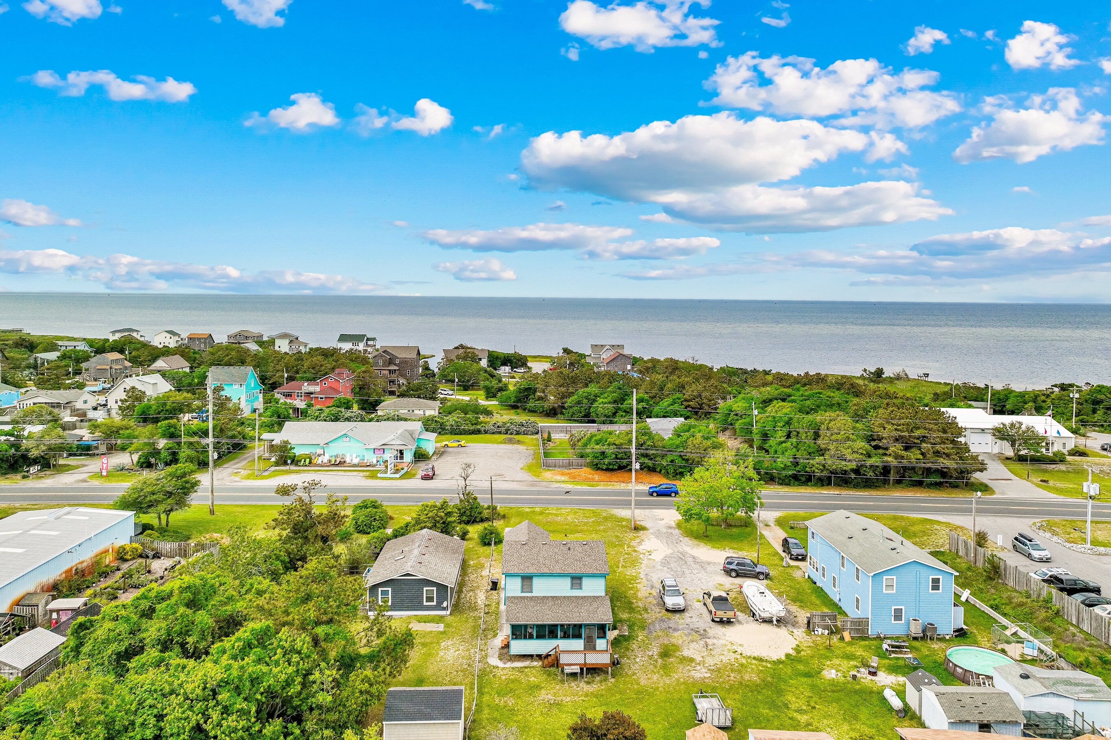 A coastal residential area with houses, a road, and a body of water in the background.