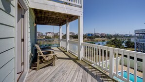 A wooden deck with a pool, a covered area with chairs, and a view of a lake and buildings in the background.