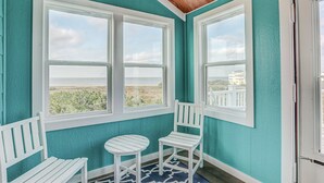 A room with teal walls, white-framed windows, a wooden ceiling, a white bench, and a small round table.