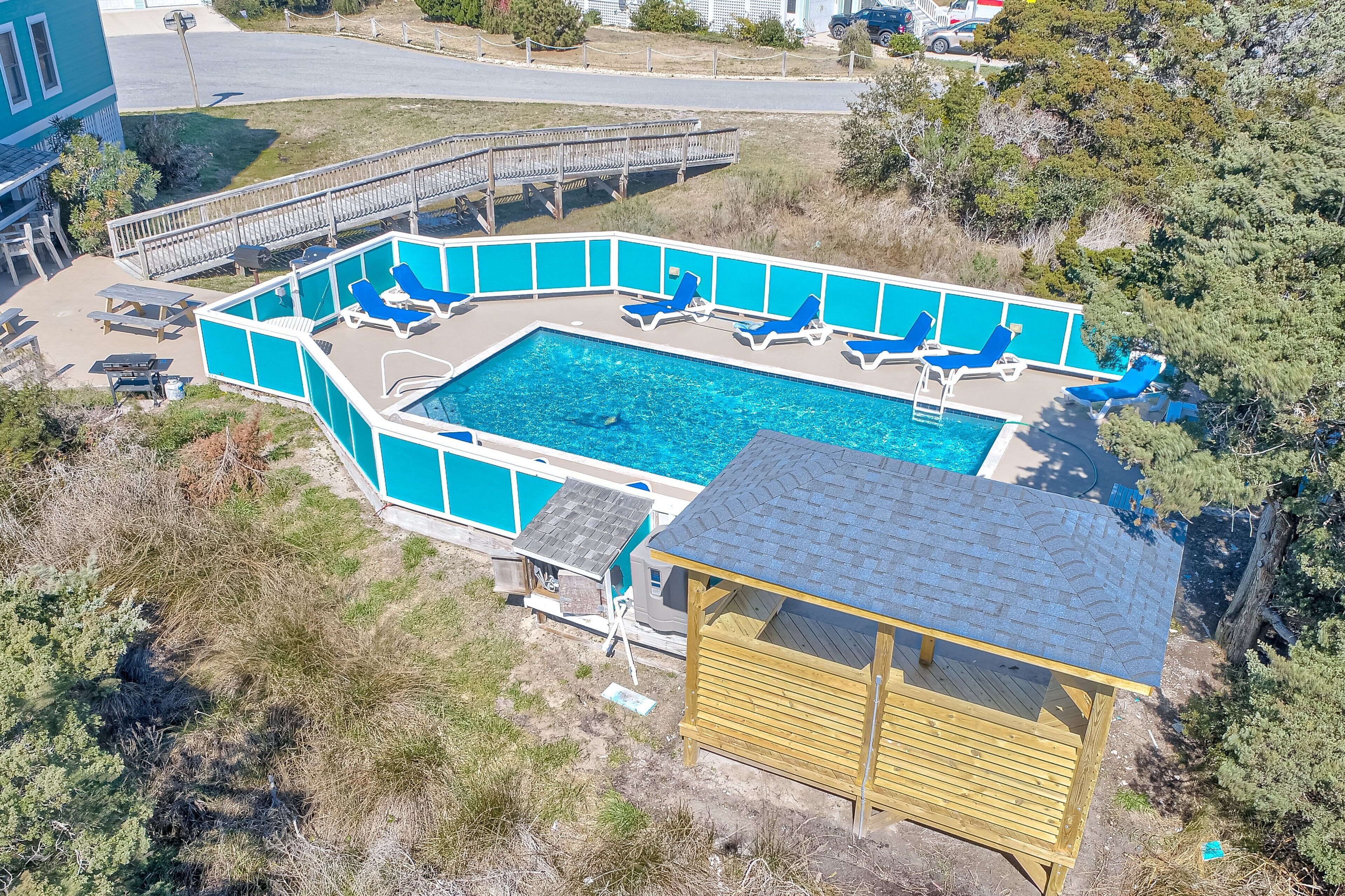A swimming pool with blue lounge chairs, a wooden deck, and a small wooden building.