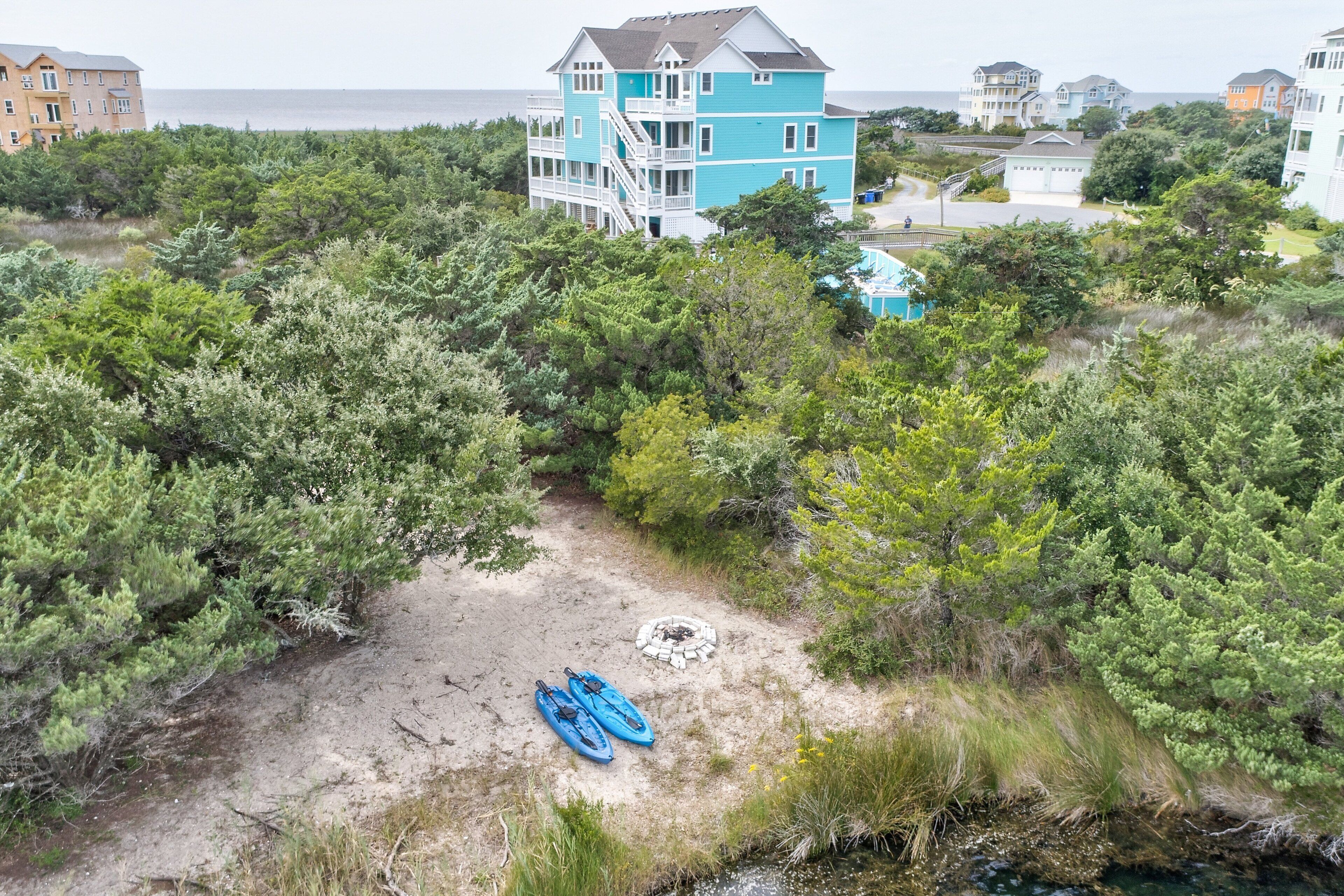 A coastal property with a large blue house, a sandy path, and kayaks.